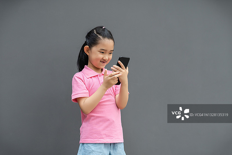 小女孩在灰色背景下使用智能手机图片素材