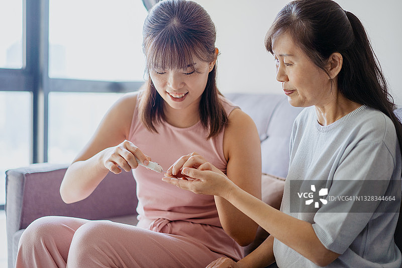 亚洲妇女帮助她的母亲在家里检查血糖水平图片素材