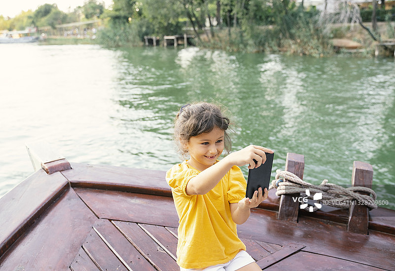 可爱的小女孩在夕阳下划着小船，玩着智能手机图片素材