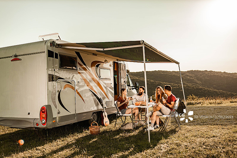 夏日里，快乐的朋友们在野营拖车旁的野餐桌上交流。图片素材