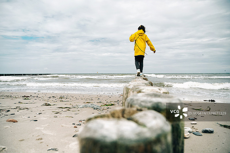 穿着黄色雨衣的小女孩走在海滩的防波堤上图片素材