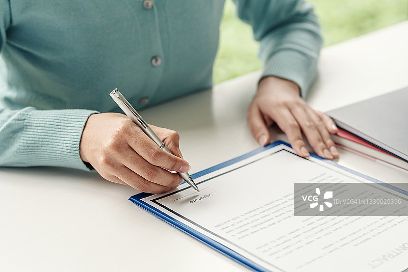 特写房地产经纪人手指着客户手里拿着笔签合同的时候正在签字。“n图片素材