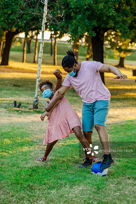 在冠状病毒时代，快乐的非洲裔父亲和女儿在户外玩足球。图片素材