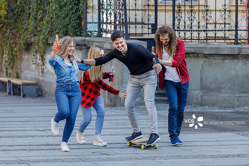一群兴高采烈的年轻人一边喝着冷饮，一边在街上散步和玩滑板。图片素材
