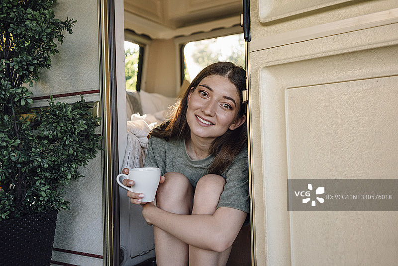 漂亮的女人拿着咖啡杯坐在露营门口图片素材