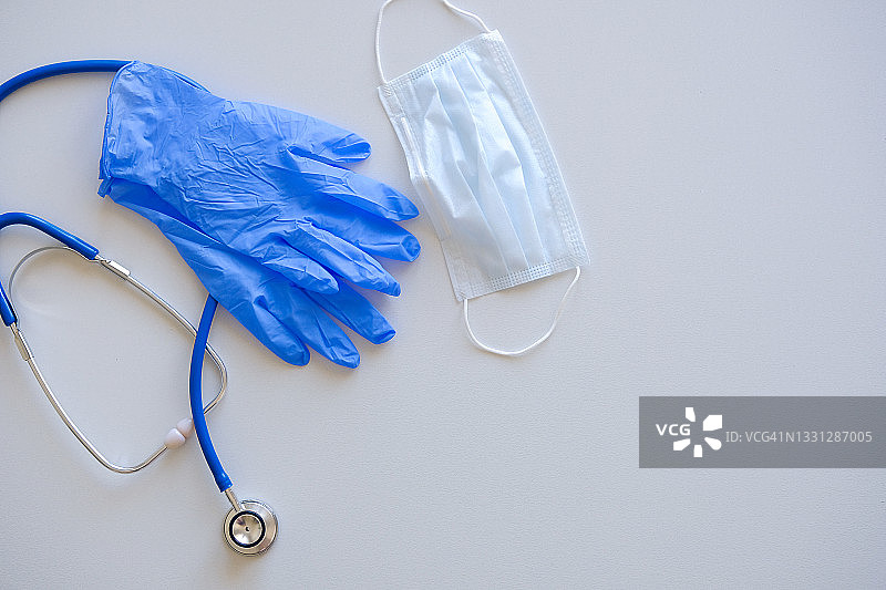 医生的听诊器在白色背景或桌面上。旁边是医用外科口罩，乳胶手套。医学和保健的概念。图片素材