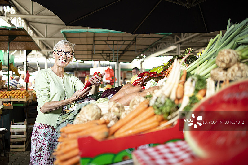 老年妇女在市场上手持并购买有机蔬菜的肖像。图片素材