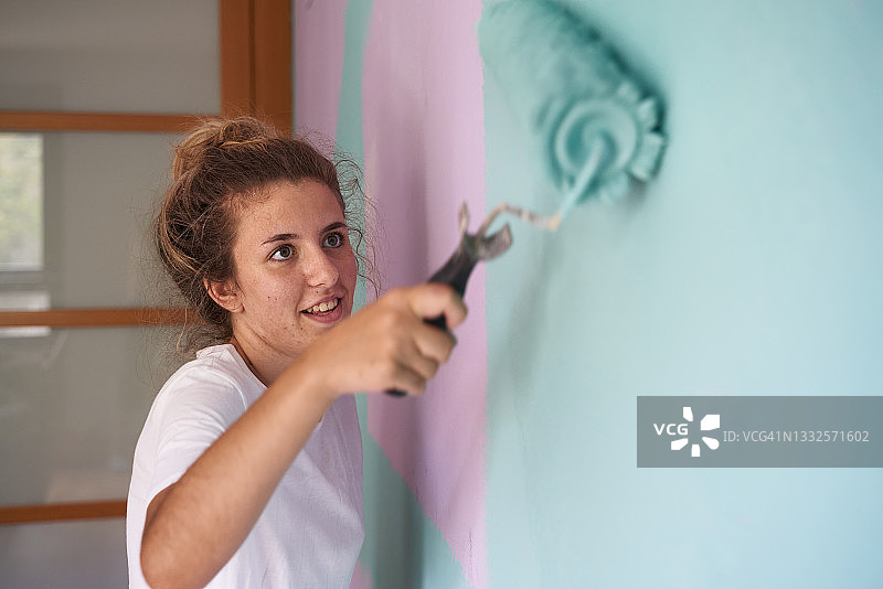 白人青年画家用油漆滚筒画房间墙壁的侧面肖像图片素材