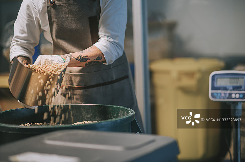 亚洲华人高级工作人员将生咖啡豆从桶中舀到秤机上，并将其混合在工厂仓库的咖啡烘焙过程中图片素材