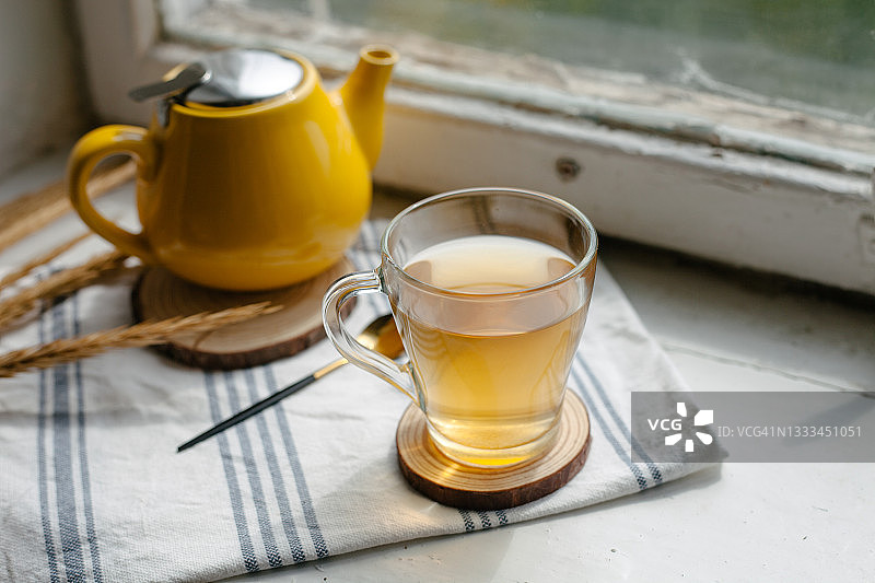 窗台上摆放着黄色的茶壶和装有花草茶的玻璃杯。图片素材