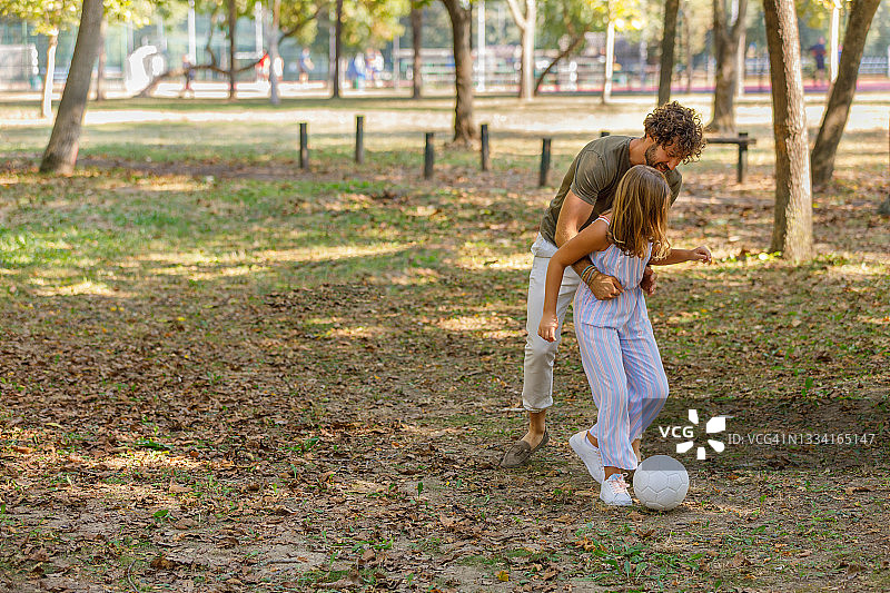 快乐的父亲和女儿正在享受大自然和踢足球。图片素材