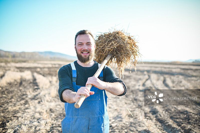 微笑的男农夫在农场拿着干草叉图片素材