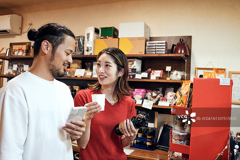 一对年轻夫妇在一家咖啡烘焙店边看手机上的信息边挑选产品图片素材