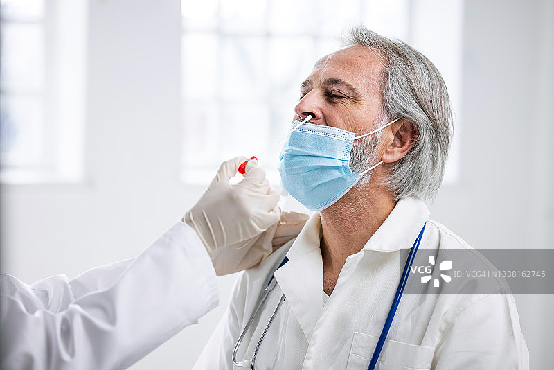 50多岁的男医生正在接受同事的鼻孔取样图片素材