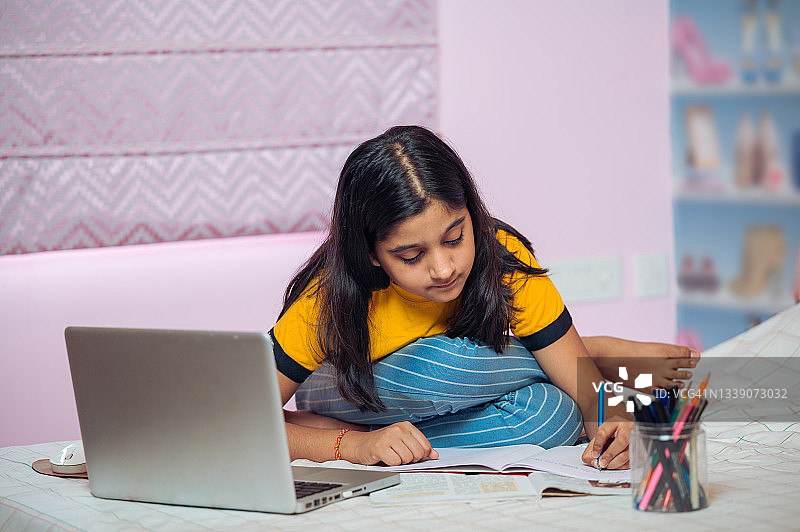 小女孩在床上用笔记本电脑和智能手机学习。图片素材