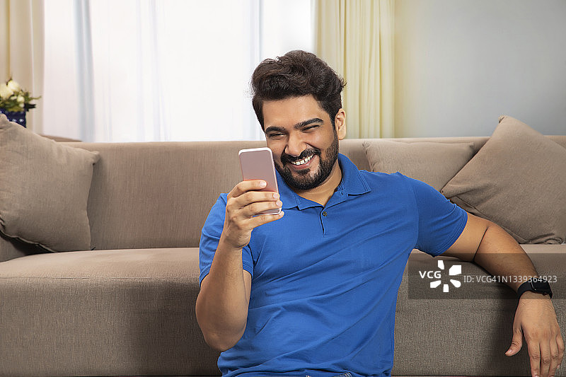 一个快乐的男人坐在家里看他的手机。图片素材