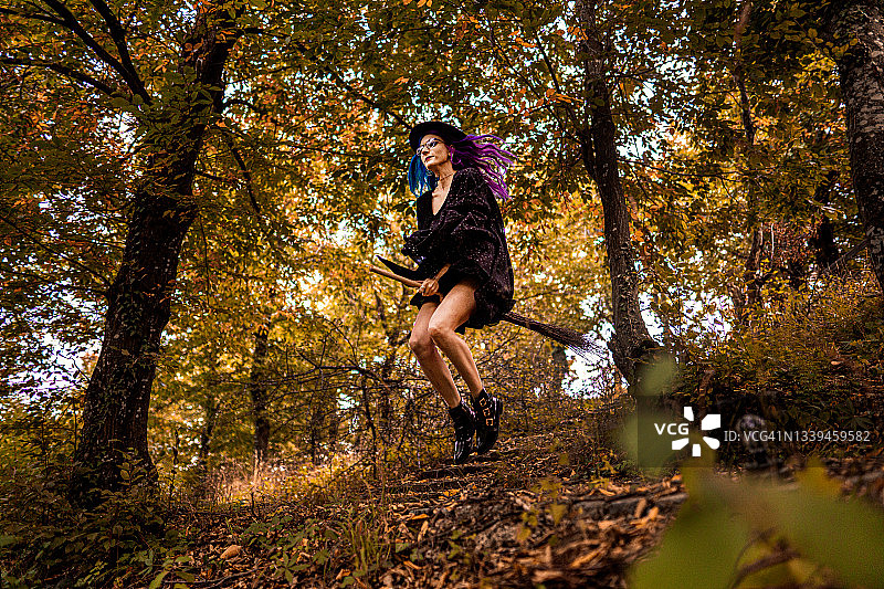 年轻的女巫骑着扫帚飞过森林图片素材