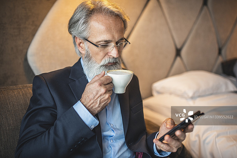 大胡子商人一边喝咖啡一边查看智能手机图片素材