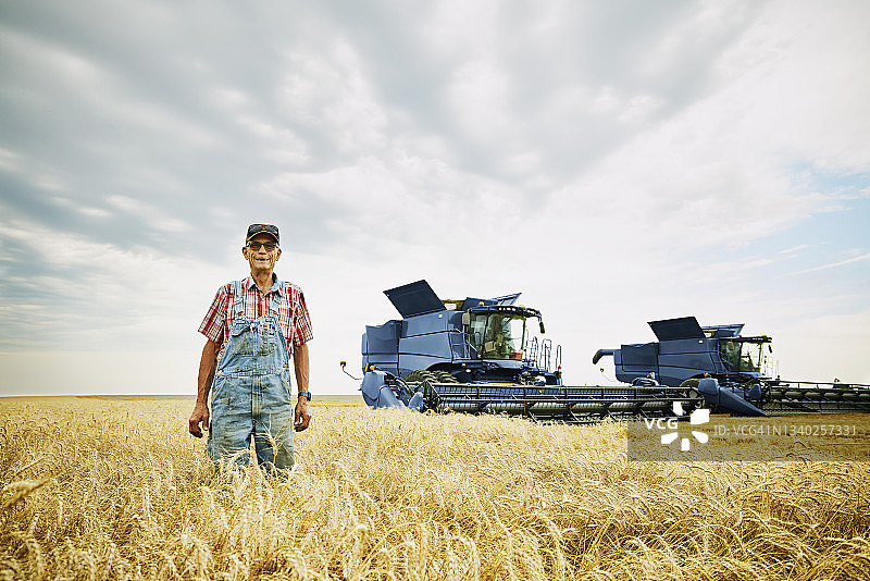 在夏季收获期，微笑的农民站在联合收割机前的麦田里图片素材
