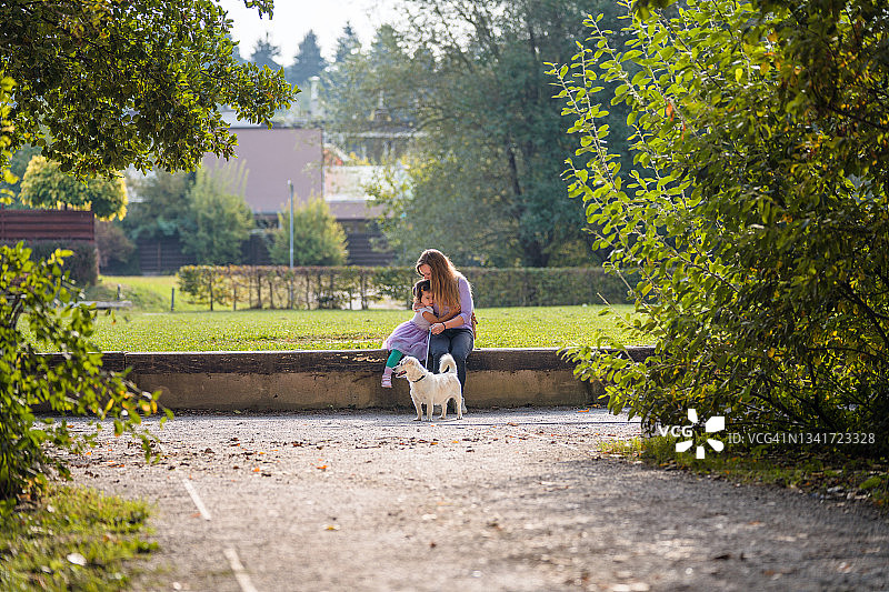 女儿和母亲带着狗坐在公园里图片素材