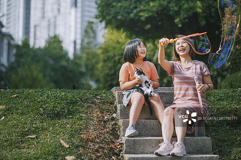 周日早上，亚洲华人妈妈和女儿在后院和猫玩泡泡，在闲暇时间聚在一起图片素材