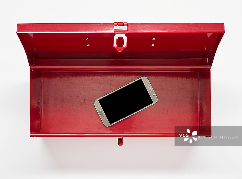 俯视着白色背景下一个红色打开的工具箱，里面有一部手机图片素材