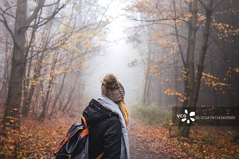 背着双肩包，戴着针织帽的女人在雾气缭绕的树林里徒步旅行图片素材