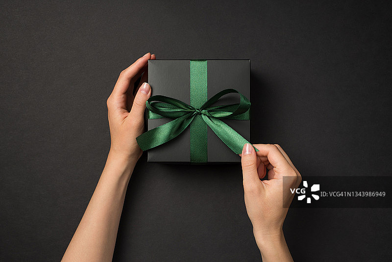 第一人俯视图照片的手打开黑色礼品盒与绿色缎带蝴蝶结孤立的黑色背景图片素材