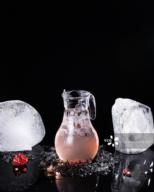 一壶柠檬汁，石榴和丁香，黑色背景和冰块图片素材