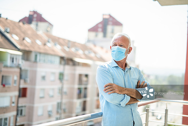 新冠肺炎大流行期间，一名戴着防护口罩的老人在阳台上的肖像。图片素材
