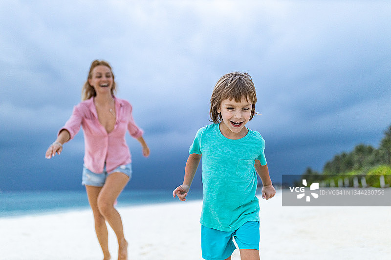 快乐的妈妈和儿子在沙滩上追逐嬉戏。图片素材