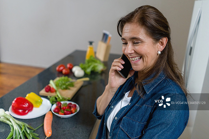 快乐的女人一边在家做饭一边打电话图片素材