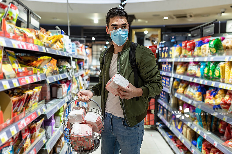 一名戴口罩的男子在超市购物。保护和预防措施。图片素材