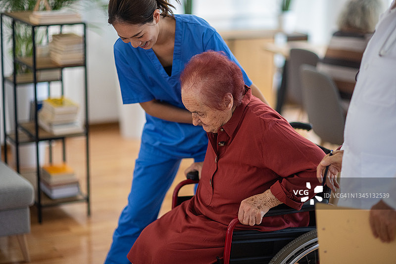 在养老院，女护士帮助老年妇女从轮椅上站起来图片素材