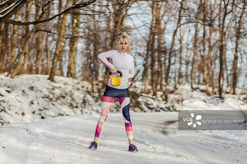 强壮的女运动员在雪天站在大自然中举起壶铃。健身，健康生活，户外健身图片素材