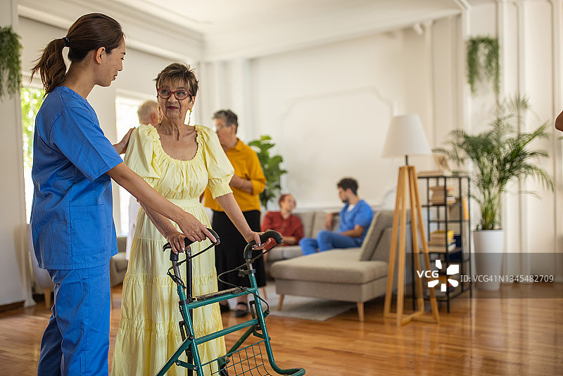 护理员协助老年妇女在养老院使用助行器行走图片素材