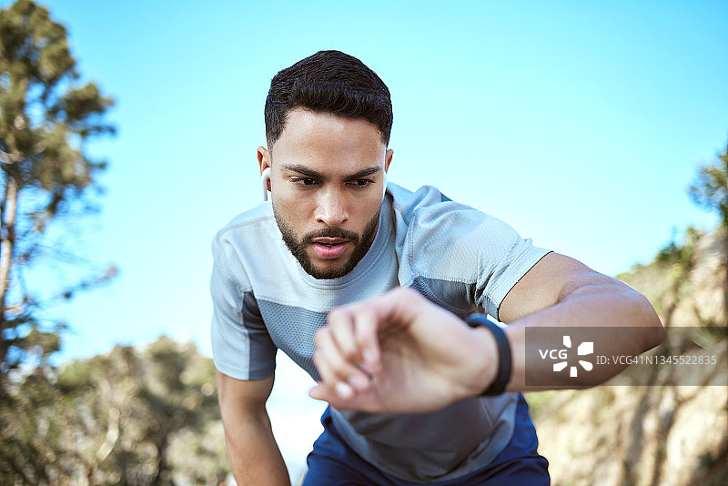 一个运动的年轻人在户外锻炼时检查他的手表图片素材
