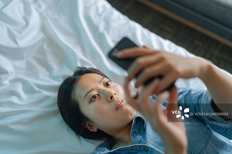 年轻女子躺在床上使用智能手机的高角度照片图片素材