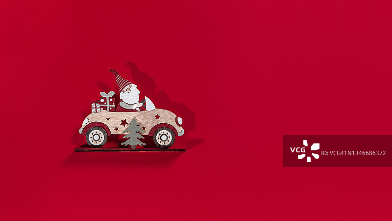 圣诞老人在一辆红色背景的车里，车上有一棵树和一份礼物。新年的概念图片素材