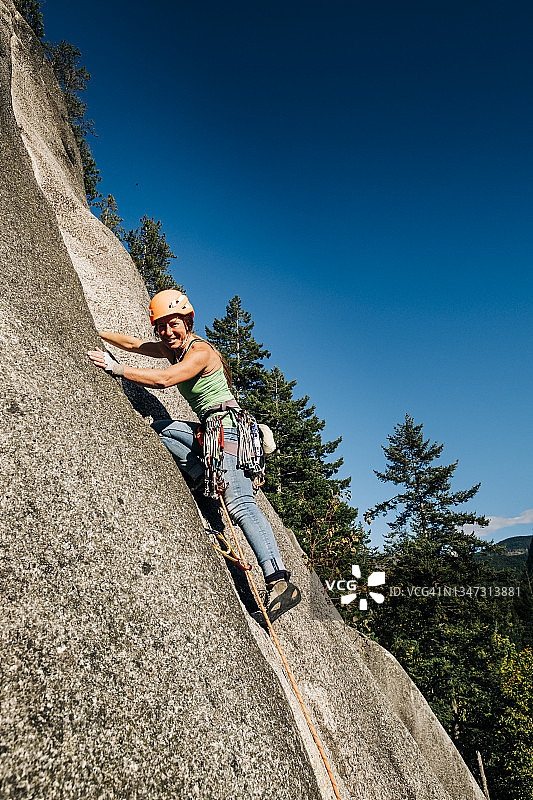 一名强壮的女攀岩者往下看，她爬上了一个又高又难爬的悬崖图片素材