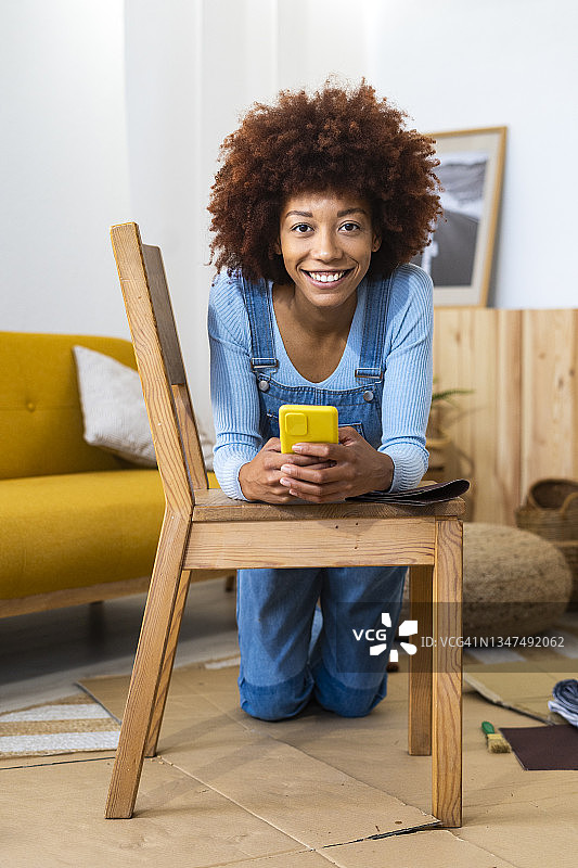 红发女人拿着智能手机倚在家里的椅子上图片素材