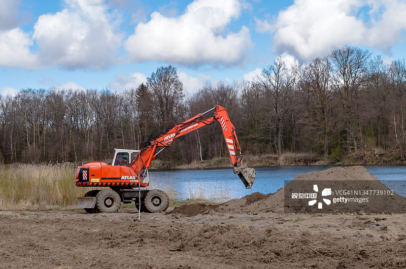挖掘机在挖土。池塘岸边的施工设备。改善海岸线。图片素材