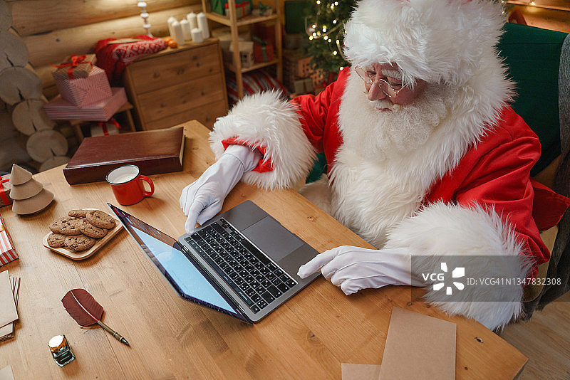 圣诞老人坐在书桌前，在书房的笔记本电脑上打字图片素材