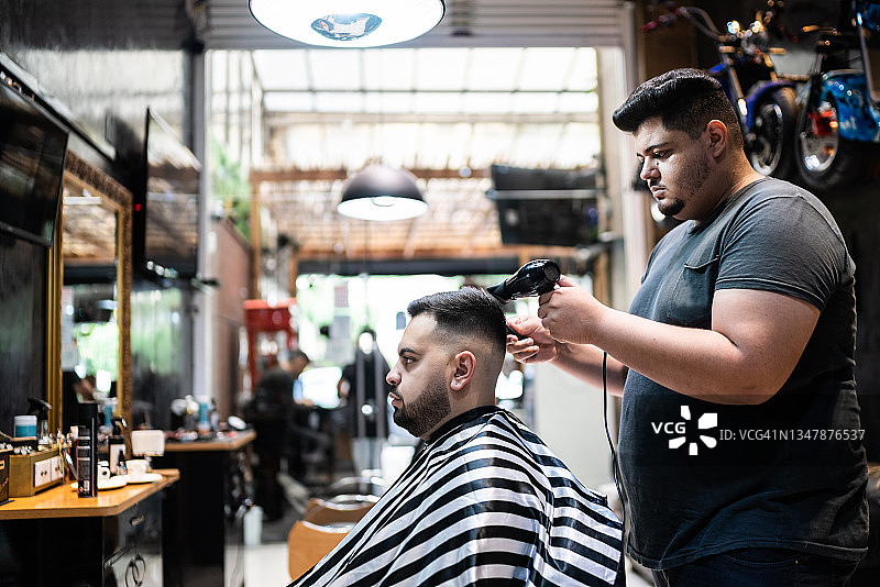 理发师在理发店里吹干一个中年男子的头发图片素材