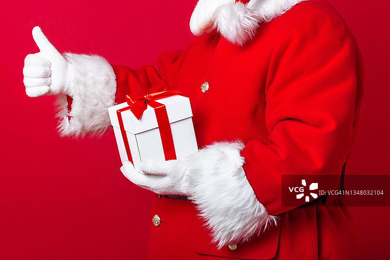 带礼物的圣诞老人在红色背景上竖起大拇指。新年和圣诞节的概念图片素材