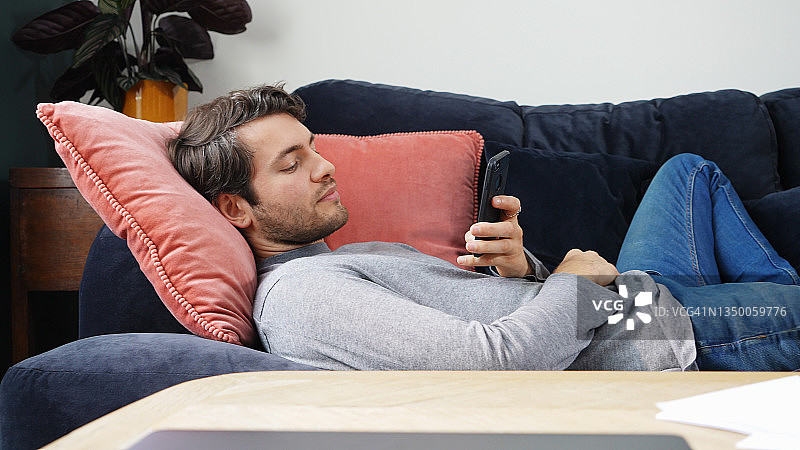 躺在沙发上看智能手机的男人图片素材