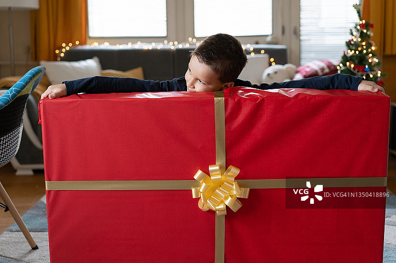 一个小男孩试图够到一份非常大的圣诞礼物的两端图片素材