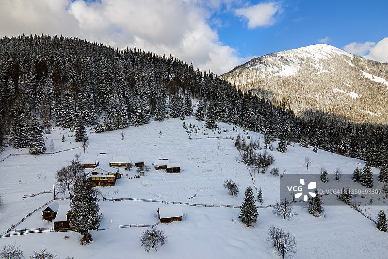 空中冬季景观与小乡村房屋之间的雪覆盖森林在寒冷的山。图片素材