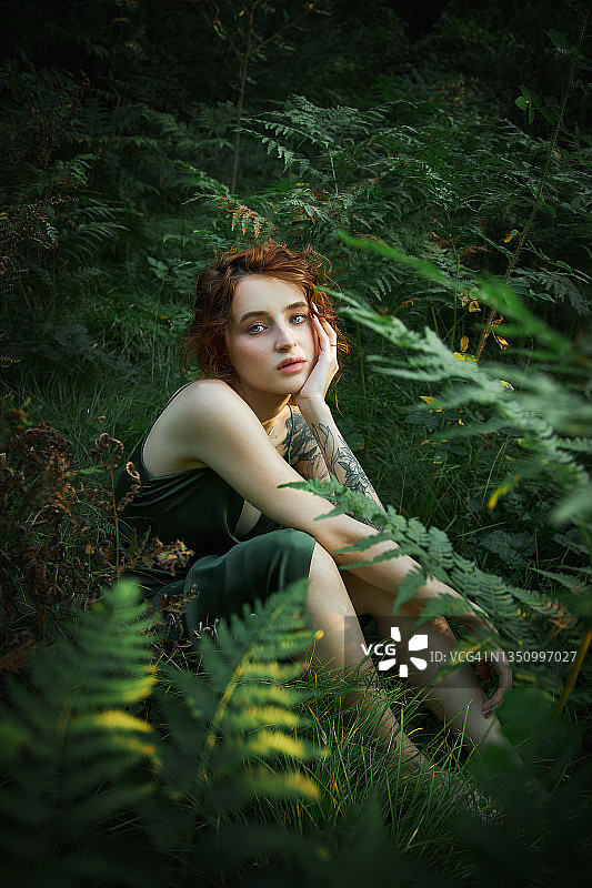 森林里一棵蕨类植物上的女人的浪漫肖像。艺术女人的自然妆容在自然中休息。绿色的蕨类植物灌丛图片素材