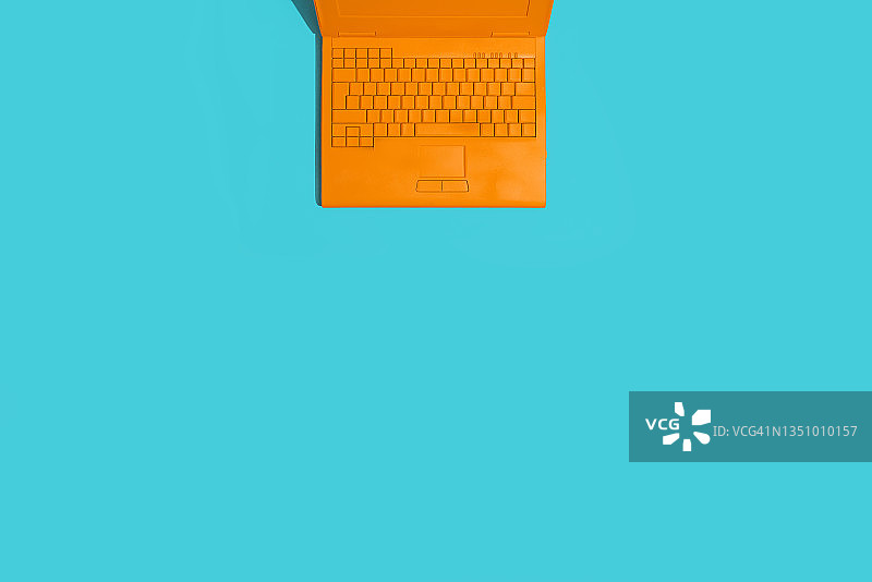 蓝绿色背景上的橙色笔记本电脑图片素材